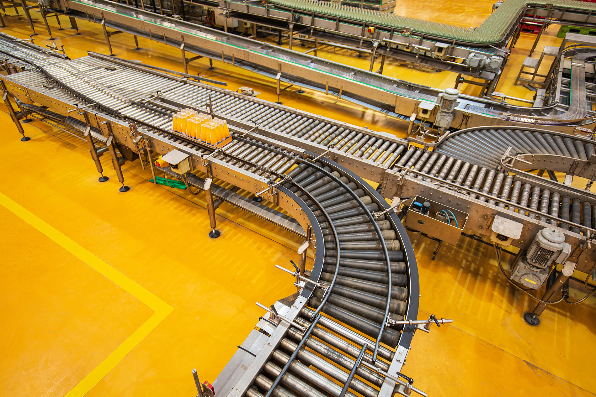 A view of an industrial conveyor system in a factory, with curved and straight roller tracks, transporting yellow plastic containers on a shiny yellow floor—ideal for showcasing Structural Analysis Services in Canada.